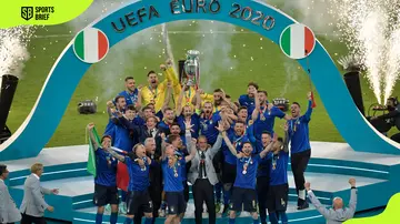 Italy's Giorgio Chiellini holds the trophy while the Italian team celebrates their victory