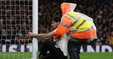 A pitch invader sits and holds on to a goal post during the English Premier League football match between Arsenal and Liverpool at the Emirates Stadium. (Photo by Adrian DENNIS / AFP)