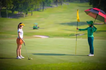 Woman golf player with caddy mate in motion going to putting a golf ball into hole on the green course