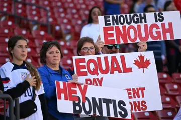 Fans hold signs in support of the Canadian women's football team's equal pay demand ahead of Canada's SheBelieves Cup match against Japan