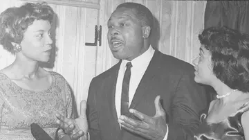 Archie Moore, an American professional boxer and the longest reigning Light Heavyweight World Champion of all time, standing with two women, speaking
