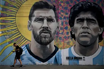 A man passes in front of a mural depicting Argentina's two greatest ever football stars, Lionel Messi (left) and Diego Maradona