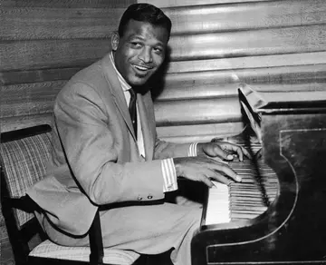 Sugar Ray Robinson (1921-1989), wearing a suit, plays a piano in his hotel room, London.