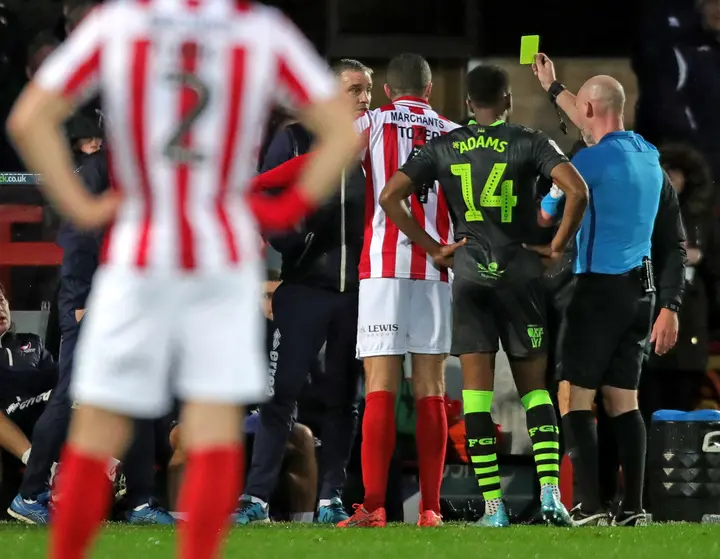 A referee issues a yellow card to Cheltenham Town's manager, Michael Duff